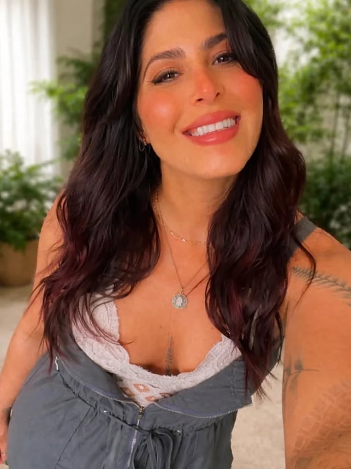 Jessica Mignone — woman with long dark wavy hair smiling at camera, wearing gray top with white lace trim and pendant necklace