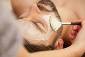 Person applying white face mask with brush to chin and cheek area during skincare routine