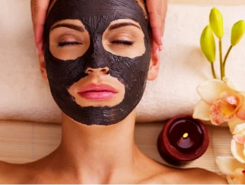 Woman wearing a black face mask at a spa with orchid flowers, candle, and towel in the background